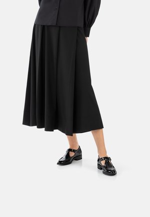 Gonna midi plissettata nera abbinata a scarpe T-bar nere lucide con un design a taglio e una fibbia decorativa.