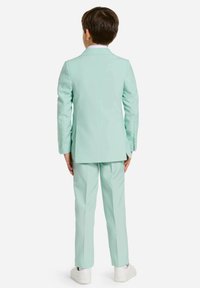 Completo verde menta con un design su misura, caratterizzato da un giubbotto a un petto e pantaloni coordinati, completato da sneakers bianche.