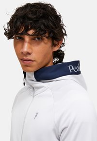 Weißes Kapuzensweatshirt mit einem marineblauen Kragen, ausgestattet mit einem grauen Logo auf der Brust und einem Reißverschluss vorne, weiche Textur.