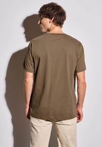 Olivově zelené tričko z měkké bavlny s kulatým výstřihem a krátkými rukávy, pohled zezadu. Mírně volný střih, hladká textura, minimalistické detaily.