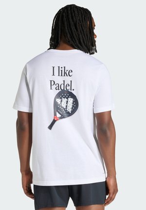 Hombre con rastas lleva una camiseta blanca con el texto "Me gusta el Padel." y un gráfico de una pala de padel en la espalda, combinado con pantalones cortos negros.