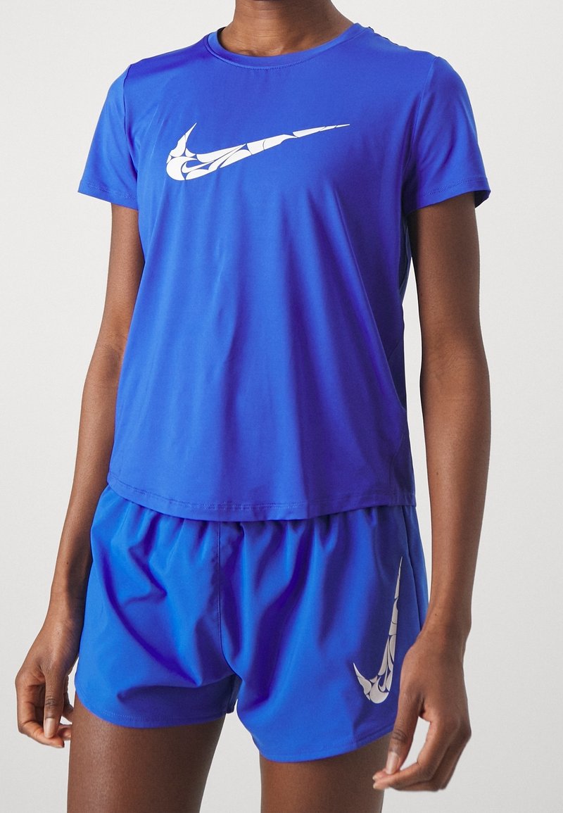 Primer plano de una persona que lleva una camiseta atlética azul brillante de Nike y pantalones cortos, con logos de swoosh blancos en el shirt y la pierna.