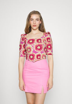 Top curto floral com mangas bufantes em rosa, amarelo e verde, combinado com uma saia mini justa rosa com uma fenda lateral. Textura suave.