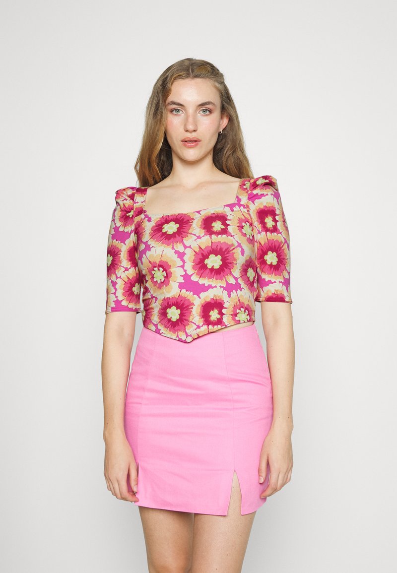 Top curto floral com mangas bufantes em rosa, amarelo e verde, combinado com uma saia mini justa rosa com uma fenda lateral. Textura suave.