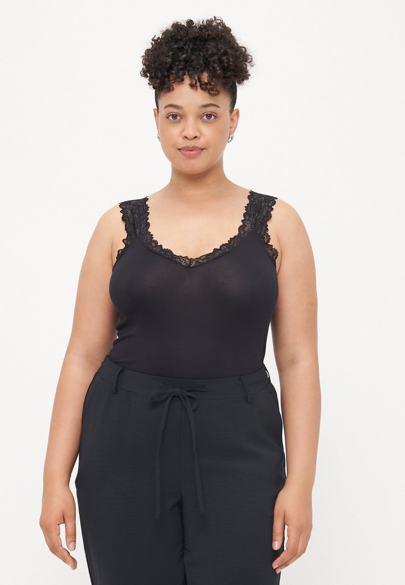 Schwarzes Tanktop mit Spitzenbesatz am Ausschnitt und den Trägern, kombiniert mit dunklen, hosen mit Kordelzug. Glatte Textur und figurbetontes Design.
