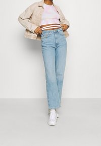 Jeans rectos de mezclilla clara combinados con una camiseta corta de tie-dye en tonos pastel y una chaqueta beige, completados con zapatillas blancas.