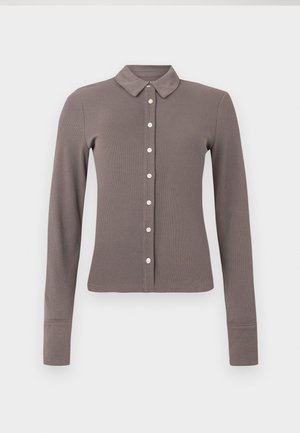 Camisa de manga larga de color marrón claro con cuello tipo polo y cierre frontal de botones. Cuenta con un sutil detalle en los puños y el dobladillo.