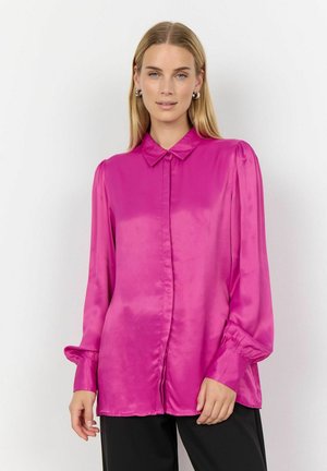 Satin pink blouse with a button-up front, soft collar, long sleeves, and gathered details at the cuffs, paired with black pants.