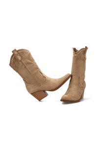 Botas de cowboy de ante color marrón claro con punta afilada, tacón cuadrado, costura decorativa y borde superior con forma de ondas. Los acentos incluyen parches de cuero en forma de triángulo.