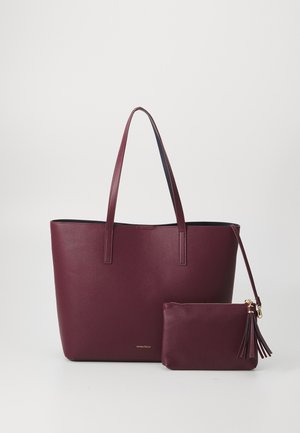 Sac fourre-tout en cuir vegan bordeaux avec deux poignées robustes, comprenant une pochette zippée assortie avec un accent de breloque. Fini lisse et texturé.