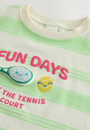 Vit kortärmad skjorta med gröna och vita ränder. Har rosa text, en grafik av en tennisracket och en broderad gul leende sol.