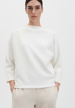 Weißes, strukturiertes Oberteil mit rundem Ausschnitt und dreiviertel Ärmeln. Verfügt über ein dezentes diagonales Muster und eine lockere Passform. Kombiniert mit hellen Hosen.