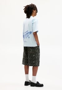 Lysblå grafisk t-shirt med et blåt spraydesign på ryggen, parret med grønne leopardprint shorts og sorte snørebåndssko.