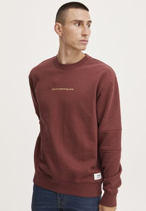 Bordeaux sweatshirt met ronde hals, lange mouwen en een textuurafwerking. Voorzien van gouden geborduurde tekst: "richt je op iets stevigs."