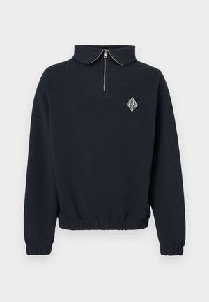 Μακρυμάνικο πουλόβερ σε ναυτικό μπλε με γιακά μισής φερμουάρ, ελαστικά μανίκια και τελείωμα, και μικρό λογότυπο σε σχήμα διαμαντιού στο αριστερό στήθος.