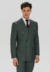 Szary, w kratę garnitur z podwójnym zapięciem, w slim fit, z klapami typu notch oraz kieszeniami bocznymi. W komplecie bordowa krawat i wzorzysty poszetka.