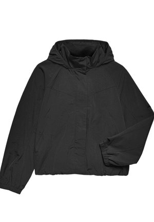Ung kvinde iført en sort jakke med elastiske manchetter og et cremefarvet skørt med sorte polkaprikker mod en neutral baggrund.