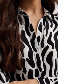 Lunghi capelli castani su una camicia a righe zebra in bianco e nero con colletto e polsini.