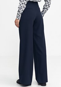 Granatowe spodnie typu wide-leg wykonane z lekkiego materiału, z dopasowanym paskiem w talii i dyskretnymi kieszeniami z tyłu. Gładka faktura i czyste linie.