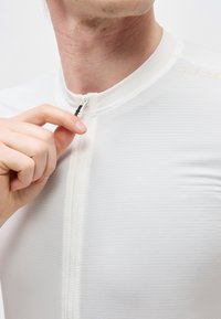 Χέρι άνδρα που τραβάει το φερμουάρ σε ένα λευκό, υφασμάτινο, εφαρμοστό πουκάμισο με ψηλό γιακά πάνω σε απλό φόντο.
