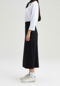 Sort midi nederdel med slim fit design. Sammen med en hvid langærmet skjorte og grå ankelsokker, kompletteret med lyse sneakers og et mønstret tørklæde.