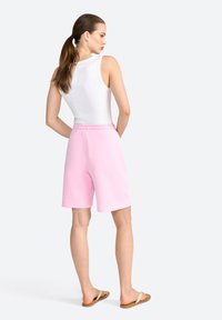 Shorts en coton rose avec une taille élastique, associés à un haut sans manches blanc et des tongs beiges, vus de dos.
