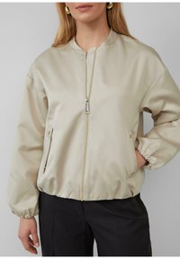 Beige satijnen bomberjack met een ritssluiting aan de voorkant, zijzakken en elastische manchetten. Gladde textuur en een casual pasvorm.