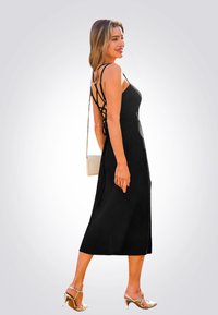 Schwarzes Midi-Kleid mit taillierter Oberseite, dünnen Kreuzgurten und strukturiertem Stoff; kombiniert mit silbernen High-Heel-Sandalen und einer kleinen Tasche.