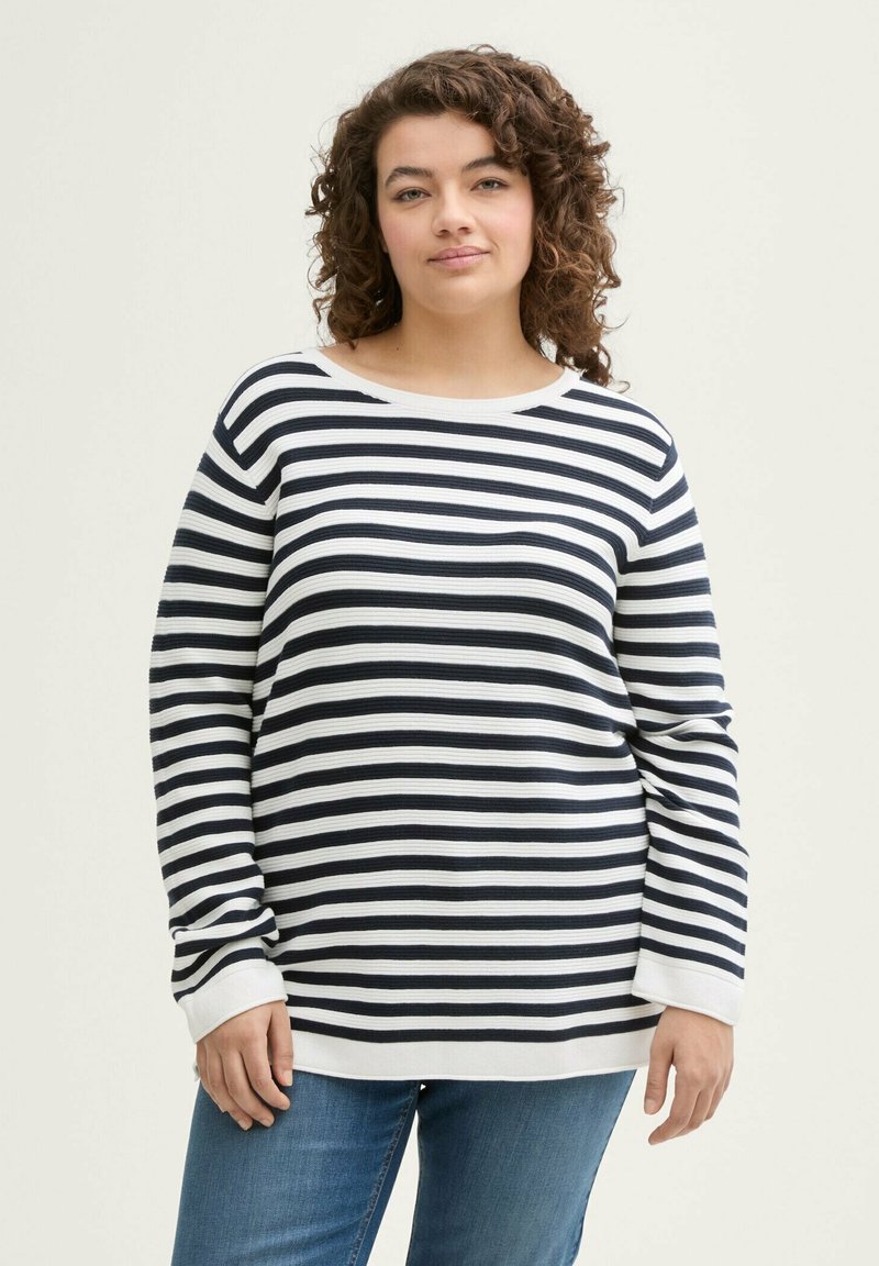 Gestreiftes Langarmoberteil in Marineblau und Weiß, aus Rippstoff gefertigt. Mit einem runden Halsausschnitt und lockerer Passform. Kombiniert mit blauen Jeans.