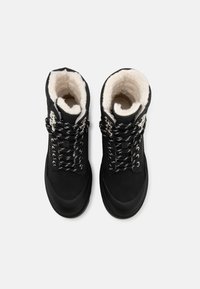 Bottes de randonnée noires avec une doublure en polaire blanche douce, dotées de lacets à motifs noir et blanc et d'œillets métalliques pour un maintien sûr.