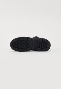 Talpa neagră de botine cu o talpă rugged, având nervuri adânci și un model texturat. Material durabil, proiectat pentru tracțiune și stabilitate.