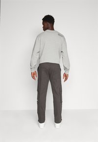 Grå sweatshirt med rund hals og grafik på ryggen, parret med mørke cargo-bukser med sidelommer. Hvide sneakers fuldender looket.