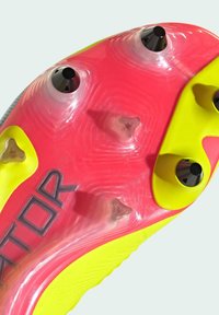 Semelle de chaussure de football avec un design éclatant en rose et jaune. Comprend des pointes moulées pour l'adhérence, des accents transparents et des rainures texturées.