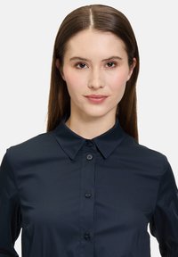 Camicia blu navy con bottoni, caratterizzata da un colletto classico, una texture liscia e sei bottoni sul fronte; maniche lunghe.