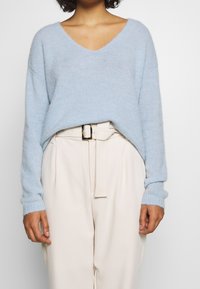Jasnoniebieski sweter z dekoltem w serek o luźnym kroju i ściągaczami na rękawach, zestawiony z kremowymi, wysokim stanem spodniami i pasującym paskiem.