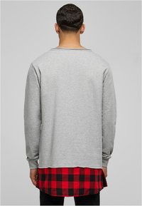 Chemise grise à manches longues avec un col rond, superposée sur une chemise en plaid rouge et noir. Matière en coton avec une texture lisse.