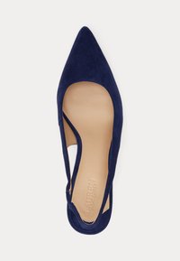 Marineblauwe suède platte slingback schoen met puntige neus en beige binnenzool waarop "Lauren Ralph Lauren" is afgedrukt, tegen een witte achtergrond.