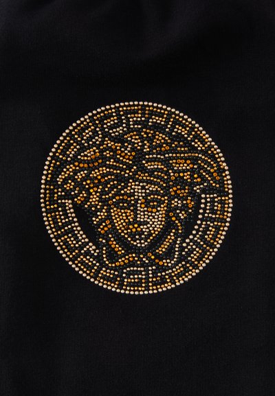 Fekete szövet kör alakú mintával díszítve, arany, ezüst és fekete swarovski kristályokkal, stilizált arcot és bonyolult mintákat ábrázolva.