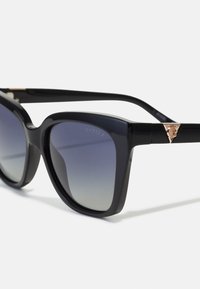 Black plastic sunglasses with large square lenses, gradient tint from dark to light, featuring a gold hardware accent near the temple.