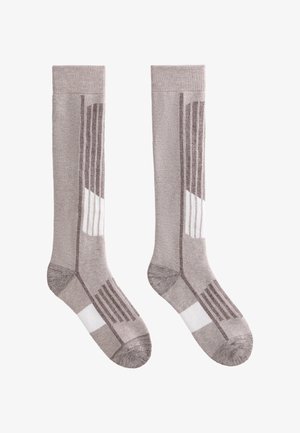 Par čarapa do koljena sive boje s tamnijim sivo-bijelim geometrijskim uzorcima na bijeloj pozadini.