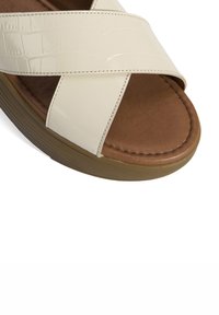 Crème-kleurige crossband sandaal met een nep-krokodillenpatroon, een bruine gevoerde voetbed en een rubberen buitenzool.