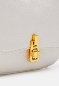 Sac en cuir blanc texturé avec une fermeture à clapet rectangulaire en or présentant un petit détail de cadenas sur le rabat avant.