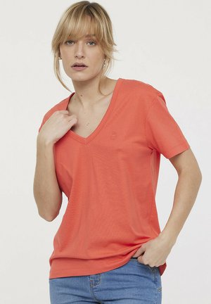 Koraal V-hals t-shirt van zacht materiaal, korte mouwen, met een reliëflogo op de borst en een losse pasvorm. Gecombineerd met blauwe jeans.