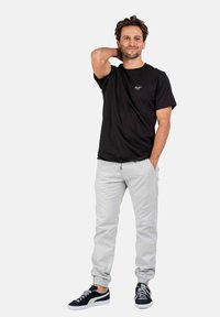 Camiseta negra, pantalones gris ajustados y zapatillas negras con suelas blancas. La tela parece suave; los pantalones tienen puños elásticos y bolsillos.