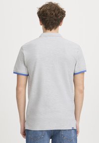 Polo gris à manches courtes, avec des accents bleus sur les poignets. Fabriqué en tissu texturé, il possède un ourlet droit et un logo de marque subtil.