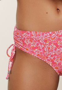 Costume da bagno inferiore rosa con motivo paisley, dettagli arricciati ai lati e lacci regolabili con accenti metallici. Texture liscia.