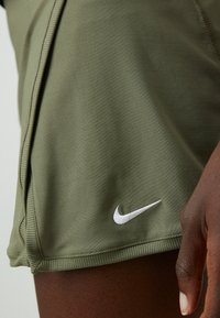 Olīvu zaļi sporta šorti, kas izgatavoti no gludas auduma. Izceļas ar baltu izšūtu Nike logo netālu no apakšējās malas un ribotām malām.