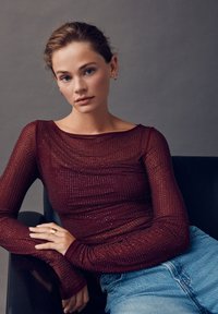 Dugotrajna bordo bluza s prozirnom teksturom i ušivenim perlicama, uparen s svijetloplavim trapericama s visokim strukom.