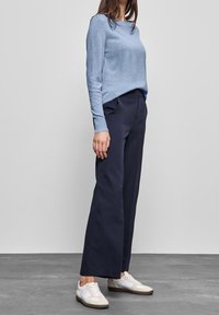 Vaaleansininen pitkähihainen neule, laivastonsiniset leveät housut ja valkoiset lenkkarit vaaleanbeigeillä sokilla. Sileä rakenne ja rento istuvuus.