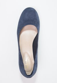Bottines plates en suède bleu marine avec bout arrondi et semelle intérieure rembourrée beige, affichant le nom de la marque en écriture dorée.